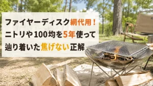 林間のキャンプ場に置いたステンレスの焚き火台と角網、手前に割った薪